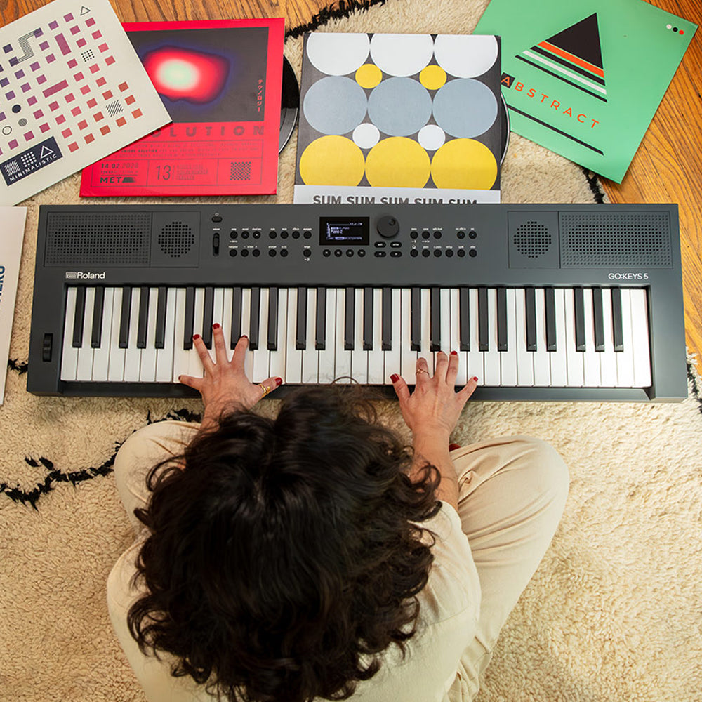Keyboard player sitting on the floor, hands playing on a Roland keyboard, with records strewn about