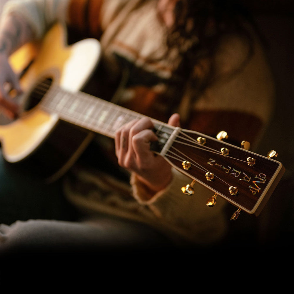 Guitar players hands on a Martin acoustic guitar fretboard and strumming the sound hole