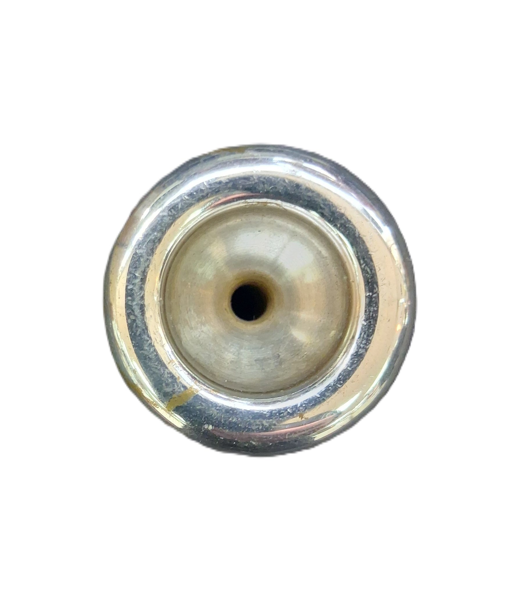 A close-up top-down view of a trumpet mouthpiece with a central hole, showing a polished silver-toned rim