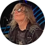 A circular portrait of Gary Grisafi wearing sunglasses and a black leather vest, photographed on a stage-like background with blue lighting.