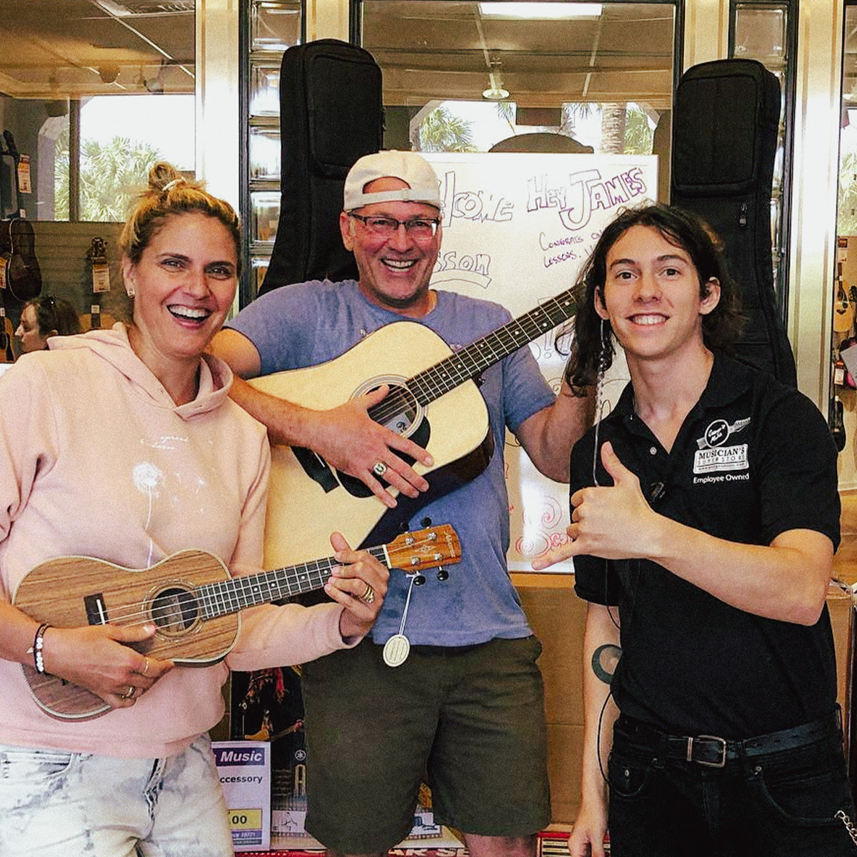 Happy customers holding acoustic guitar and ukulele inside George’s Music