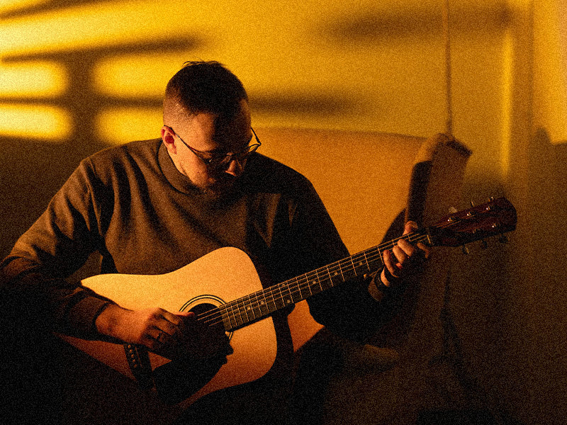 Musician playing acoustic guitar at home in warm evening lighting