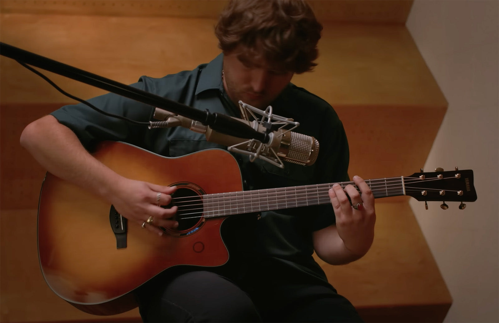 Person playing an acoustic guitar in a studio setting with a microphone.